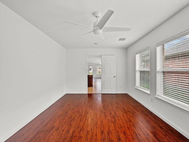 empty room featuring ceiling fan, visible vents, baseboards, and dark wood finished floors