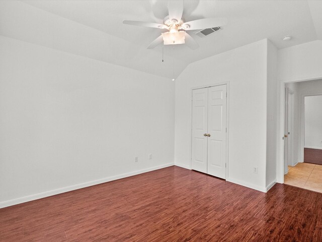 unfurnished bedroom featuring visible vents, baseboards, lofted ceiling, wood finished floors, and a closet