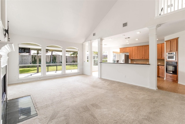 unfurnished living room featuring visible vents, light carpet, high vaulted ceiling, a fireplace with flush hearth, and decorative columns