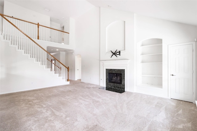 unfurnished living room featuring built in shelves, high vaulted ceiling, a high end fireplace, stairway, and carpet flooring