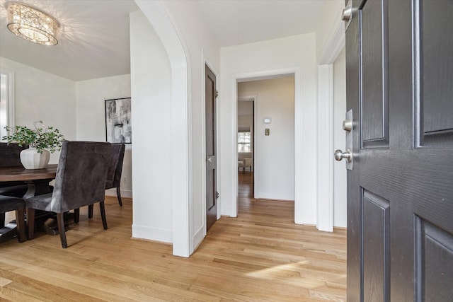 entrance foyer featuring baseboards, arched walkways, and light wood-style floors