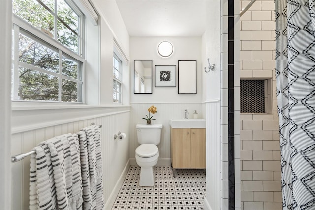 full bath featuring a shower with shower curtain, vanity, toilet, and wainscoting