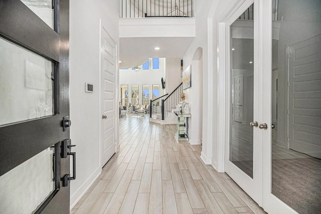 foyer with wood finish floors, stairway, french doors, baseboards, and a towering ceiling