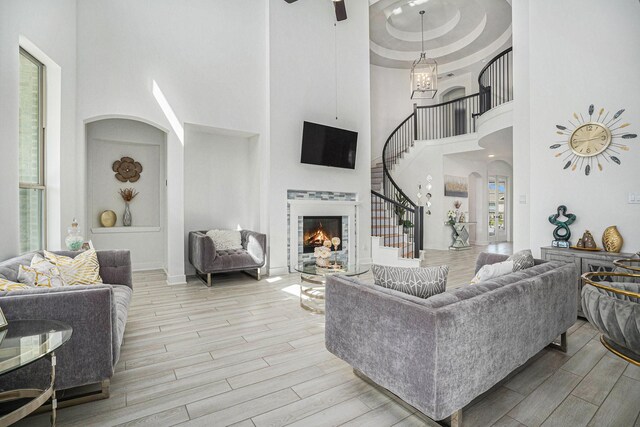 living room featuring wood finish floors, a tray ceiling, arched walkways, a lit fireplace, and stairs