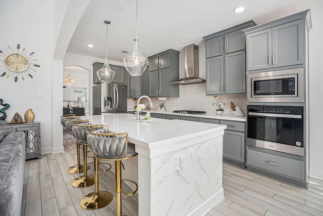 kitchen featuring gray cabinets, arched walkways, a sink, stainless steel appliances, and wall chimney range hood