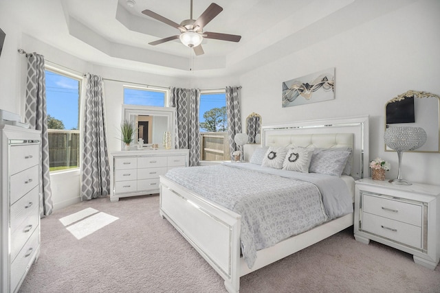 bedroom with a raised ceiling, a ceiling fan, and light carpet