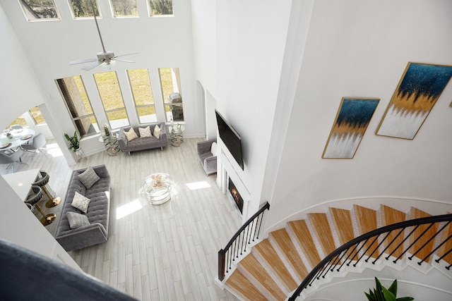 living room with a lit fireplace, stairway, a towering ceiling, and wood finished floors