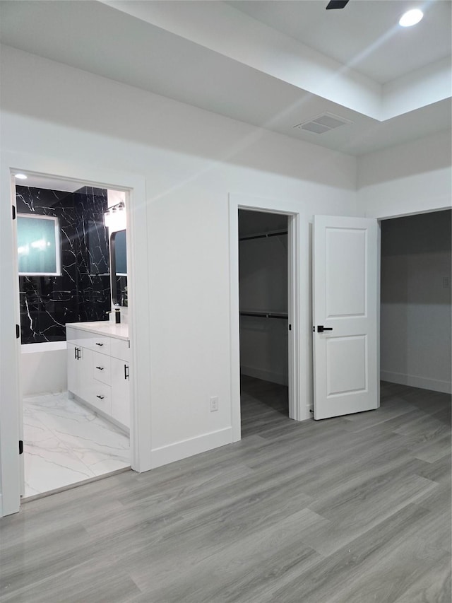 unfurnished bedroom with visible vents, ensuite bathroom, light wood finished floors, baseboards, and a spacious closet