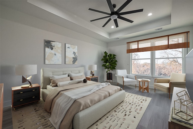 bedroom featuring a tray ceiling, recessed lighting, wood finished floors, and visible vents