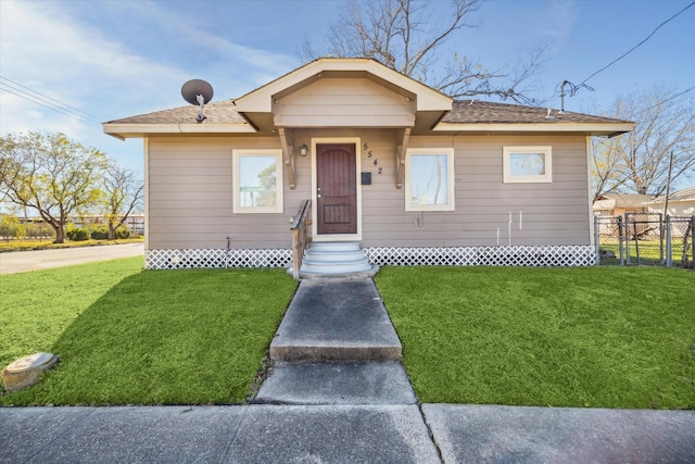 bungalow with entry steps, a front lawn, fence, and a shingled roof