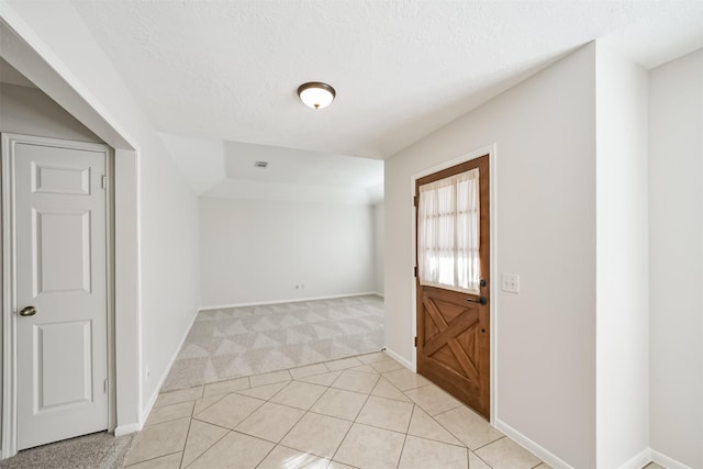 empty room featuring light tile patterned floors, light colored carpet, baseboards, and a textured ceiling