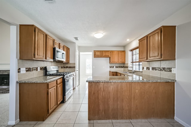 kitchen featuring visible vents, a sink, light stone counters, appliances with stainless steel finishes, and brown cabinetry