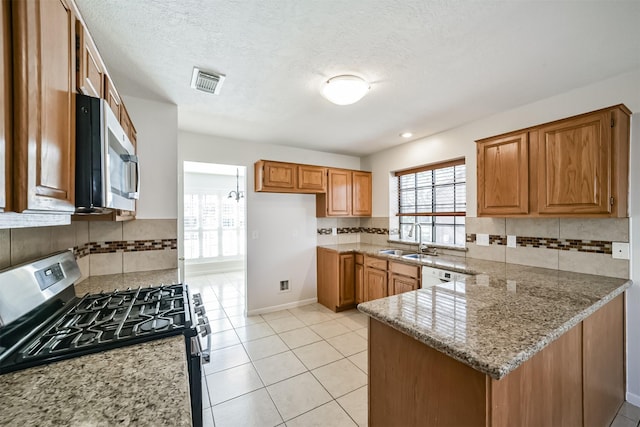 kitchen featuring brown cabinetry, visible vents, a peninsula, a sink, and stainless steel appliances