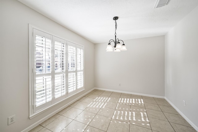 empty room with tile patterned floors, visible vents, a notable chandelier, a textured ceiling, and baseboards