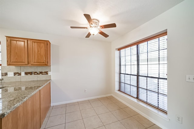 kitchen featuring backsplash, baseboards, ceiling fan, light stone counters, and light tile patterned floors