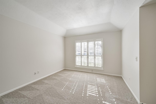 carpeted empty room featuring vaulted ceiling, baseboards, and a textured ceiling