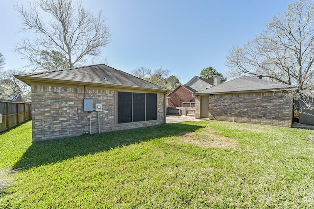 back of property featuring fence, a lawn, brick siding, and roof with shingles