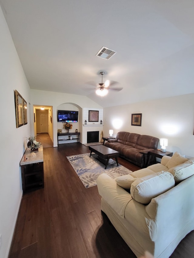 living area with visible vents, ceiling fan, vaulted ceiling, a fireplace, and dark wood-style flooring