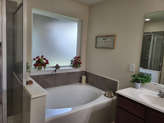 bathroom with a shower stall, vanity, a garden tub, and a textured wall