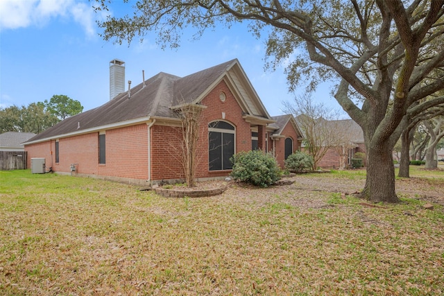 view of front of house featuring brick siding, a shingled roof, a front yard, central AC unit, and a chimney