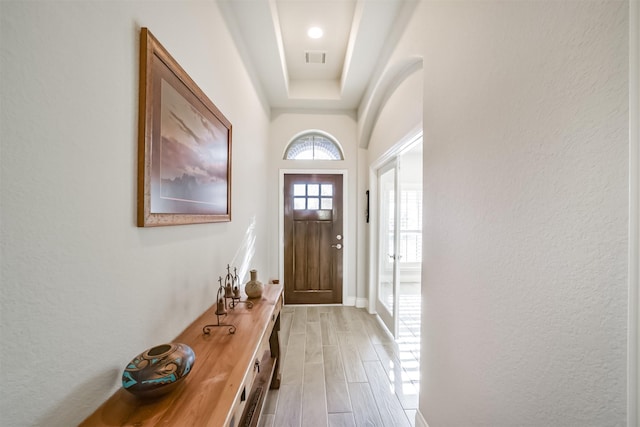 doorway with visible vents, a raised ceiling, wood tiled floor, and a textured wall