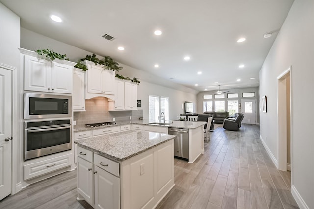 kitchen with a kitchen island, a peninsula, a sink, stainless steel appliances, and backsplash