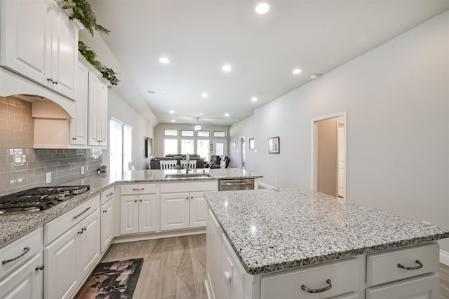 kitchen featuring a kitchen island, a peninsula, a sink, decorative backsplash, and appliances with stainless steel finishes