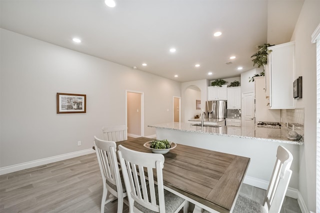 dining area featuring recessed lighting, baseboards, arched walkways, and light wood finished floors