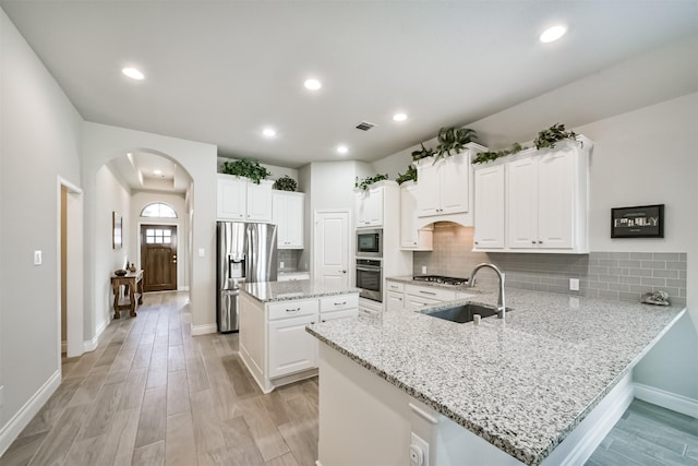 kitchen with a kitchen island, appliances with stainless steel finishes, a peninsula, arched walkways, and a sink