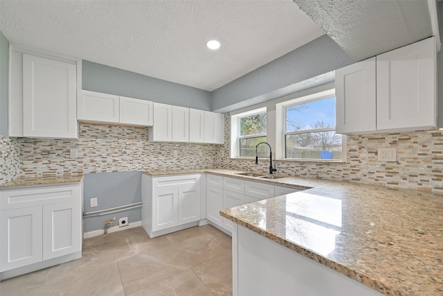 kitchen with white cabinetry, light stone counters, and a sink