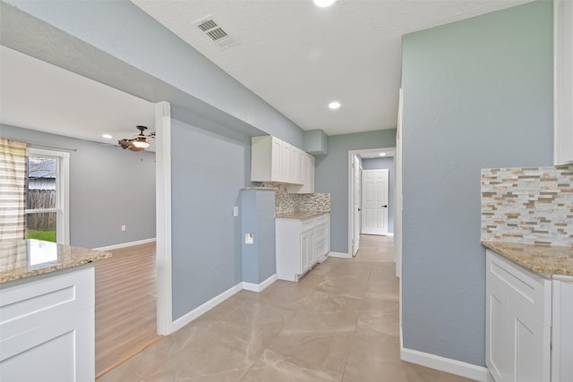 kitchen featuring tasteful backsplash, visible vents, baseboards, light stone counters, and white cabinets