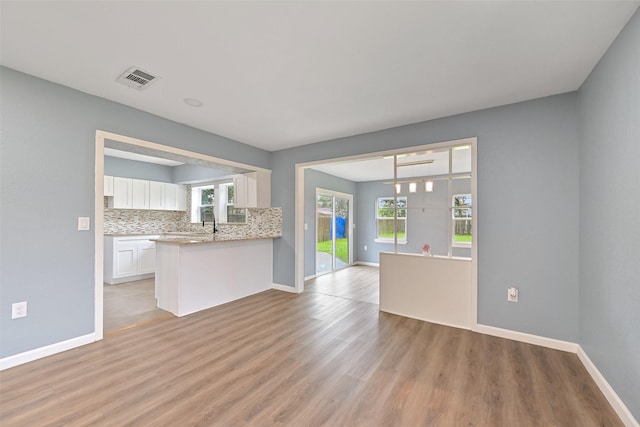 kitchen featuring light wood-type flooring, visible vents, tasteful backsplash, open floor plan, and white cabinets