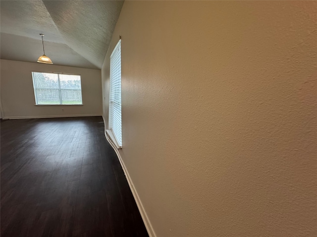 empty room featuring baseboards, dark wood-type flooring, a textured ceiling, and vaulted ceiling