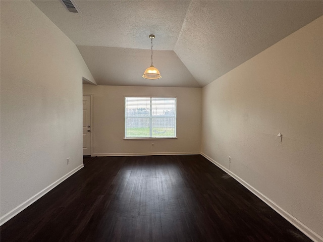 spare room with visible vents, dark wood-type flooring, a textured ceiling, baseboards, and lofted ceiling