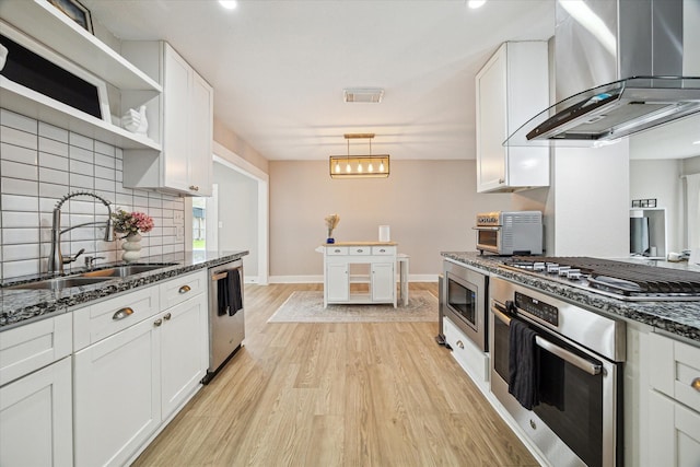 kitchen featuring visible vents, light wood-style flooring, appliances with stainless steel finishes, wall chimney exhaust hood, and a sink