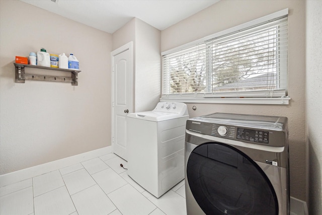 clothes washing area with laundry area, light tile patterned flooring, washing machine and dryer, and baseboards