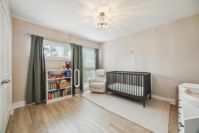 bedroom featuring a nursery area, wood finished floors, baseboards, and a chandelier