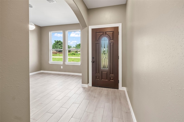 entrance foyer with light wood-type flooring, visible vents, arched walkways, baseboards, and a textured wall