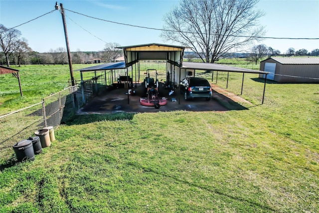 view of yard with a detached carport, an outbuilding, fence, driveway, and a rural view