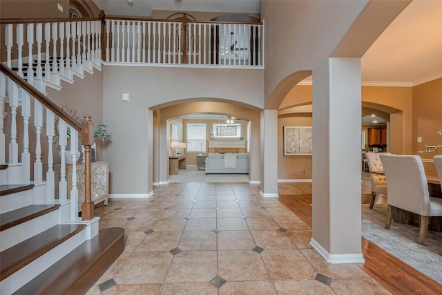 foyer entrance featuring tile patterned floors, ornamental molding, stairway, a high ceiling, and baseboards