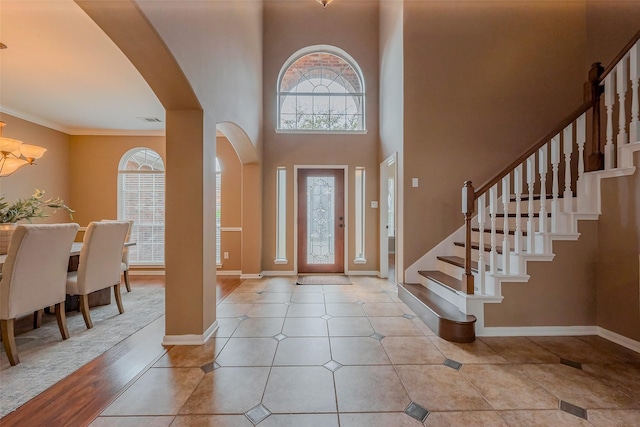 tiled foyer featuring baseboards, stairs, a high ceiling, an inviting chandelier, and arched walkways