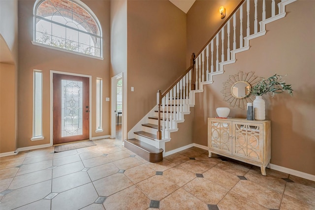 tiled foyer featuring baseboards, a high ceiling, and stairs