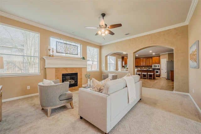 living area featuring visible vents, baseboards, arched walkways, ornamental molding, and light carpet