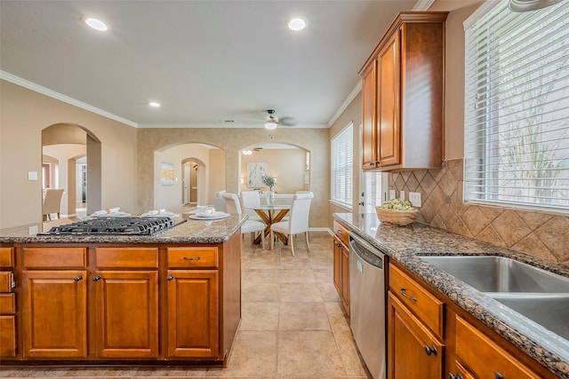 kitchen with ornamental molding, dark stone countertops, backsplash, arched walkways, and appliances with stainless steel finishes