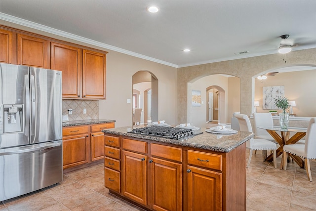 kitchen featuring brown cabinets, backsplash, a center island, stainless steel appliances, and dark stone counters