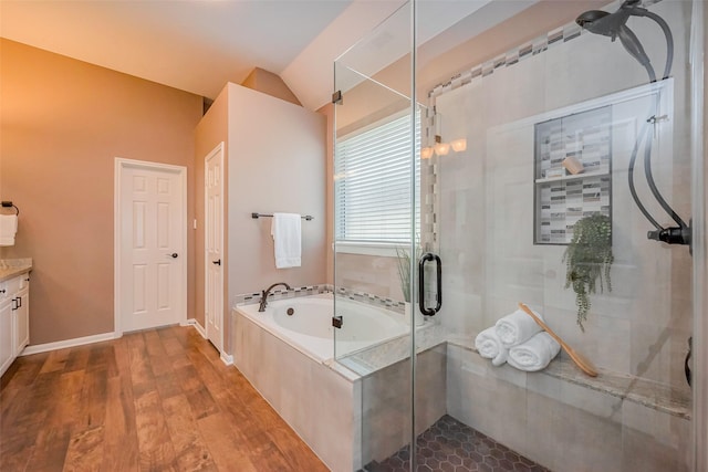 bathroom featuring a garden tub, vaulted ceiling, a stall shower, wood finished floors, and vanity