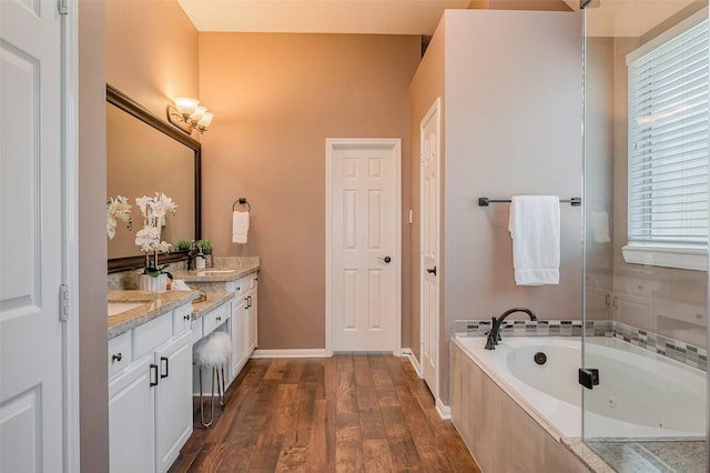 bathroom featuring baseboards, a garden tub, double vanity, wood finished floors, and a sink