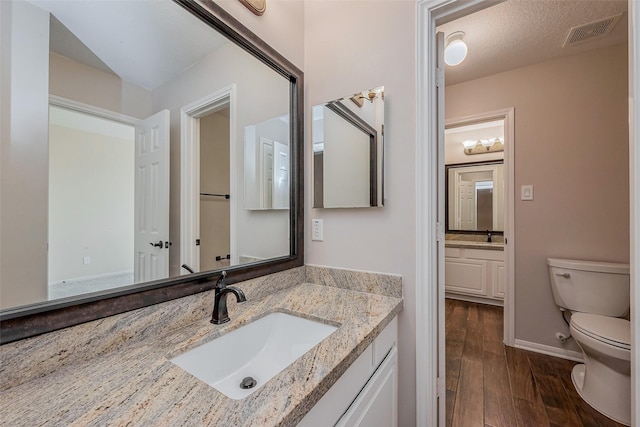 bathroom featuring vanity, wood finished floors, visible vents, a textured ceiling, and toilet