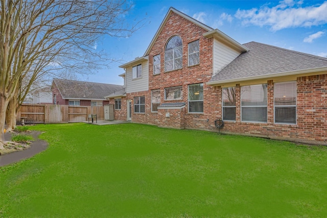 rear view of house with brick siding, fence, roof with shingles, a lawn, and a patio area