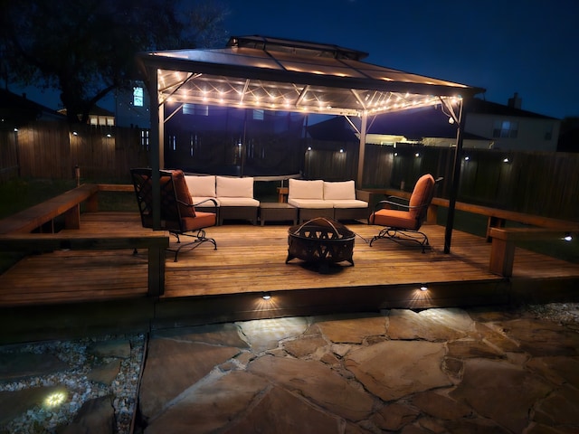 deck at night with an outdoor living space with a fire pit, a gazebo, and fence